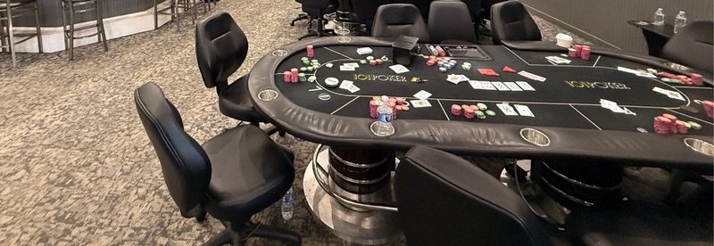 A poker table left mid-hand with chips, cards and a water bottle on the felt, with empty chairs pulled up around it