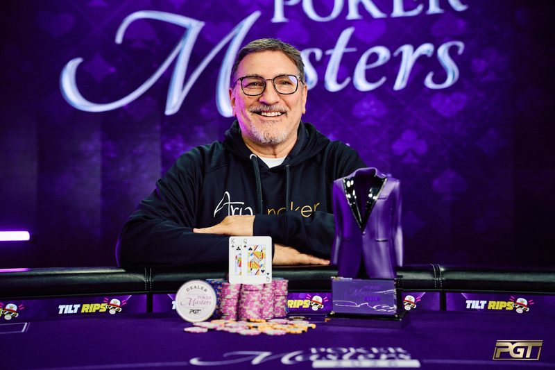 Keith Lehr in glasses and a black hoodie smiling at the winner's table behind the king and queen, a stack of chips and the purple jacket trophy