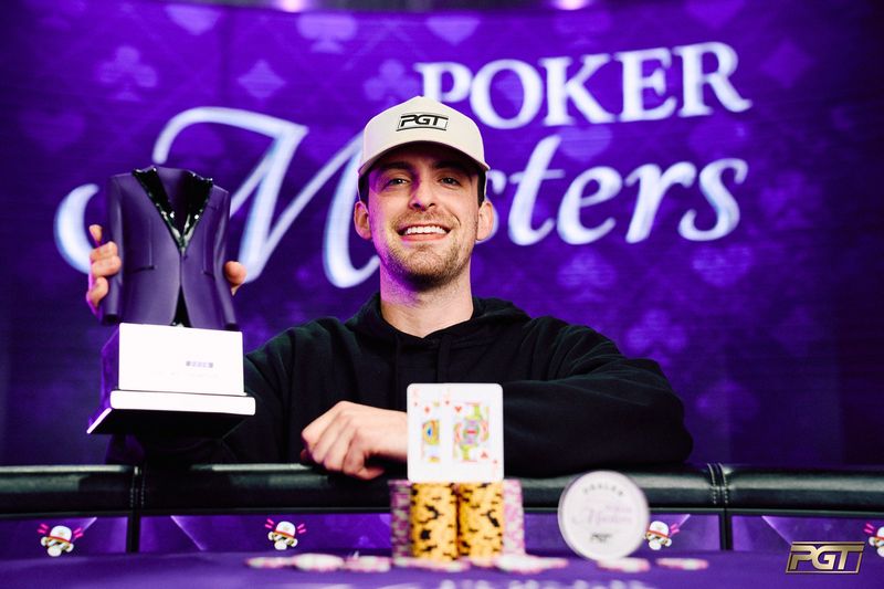 Nick Seward in a white PGT cap and black hoodie smiling behind a stack of chips and the king-jack, holding up the purple jacket trophy in front of a Poker Masters backdrop
